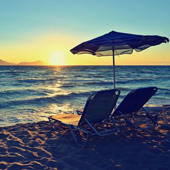 Sunbeds and umbrella on the beach at sunset by the sea. Beautiful concept for vacation, summer holidays and travel.