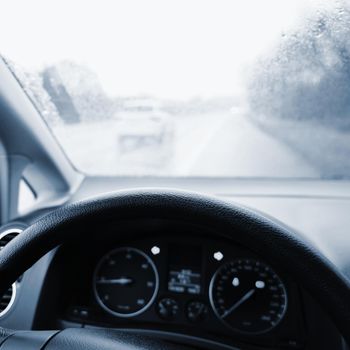 View from the driver - car interior with steering wheel and dashboard. Winter bad rainy weather and dangerous driving on the road.