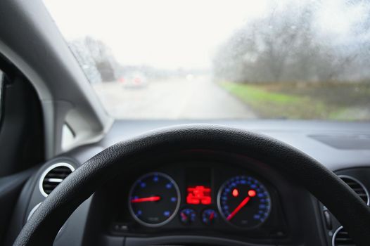 View from the driver - car interior with steering wheel and dashboard. Winter bad rainy weather and dangerous driving on the road.