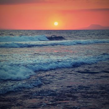 Beautiful summer sunset by the sea. Amazing scenery on the beach with waves and reflection of the sun. Background for holiday and vacation travel. Greece Crete Island.