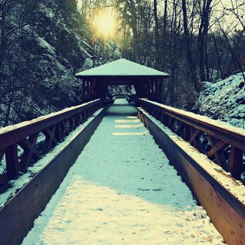 Beautiful snowy wooden bridge with a path for hiking. Winter season with snow and sun.