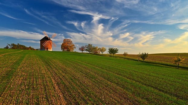 Beautiful autumn landscape with old windmill at sunset and beautiful blue sky with clouds. Colorful nature background on autumn season. Chvalkovice - Czech Republic.