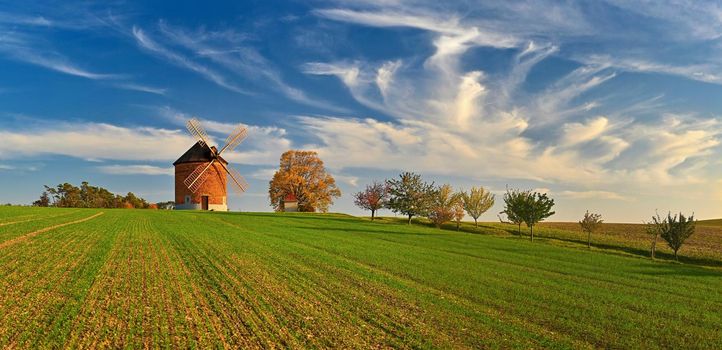 Beautiful autumn landscape with old windmill at sunset and beautiful blue sky with clouds. Colorful nature background on autumn season. Chvalkovice - Czech Republic.