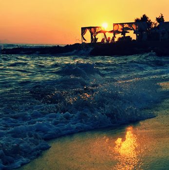 Beautiful summer sunset by the sea. Amazing scenery on the beach with waves and reflection of the sun. Background for holiday and vacation travel. Greece Crete Island.