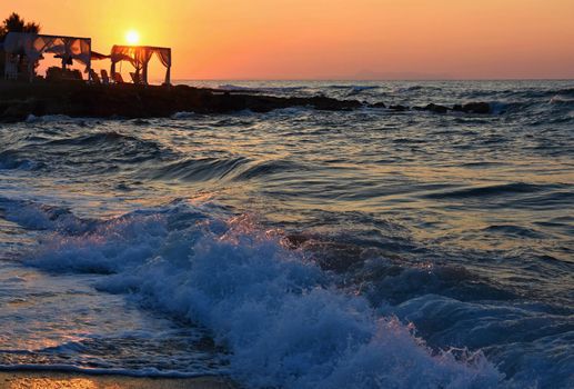 Beautiful summer sunset by the sea. Amazing scenery on the beach with waves and reflection of the sun. Background for holiday and vacation travel. Greece Crete Island.