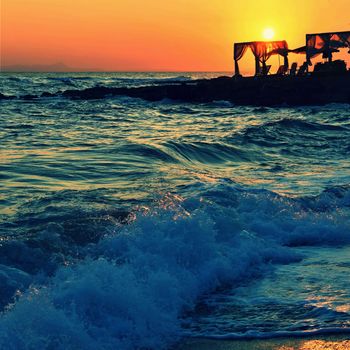 Beautiful summer sunset by the sea. Amazing scenery on the beach with waves and reflection of the sun. Background for holiday and vacation travel. Greece Crete Island.