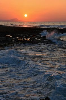 Beautiful summer sunset by the sea. Amazing scenery on the beach with waves and reflection of the sun. Background for holiday and vacation travel. Greece Crete Island.