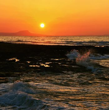 Beautiful summer sunset by the sea. Amazing scenery on the beach with waves and reflection of the sun. Background for holiday and vacation travel. Greece Crete Island.