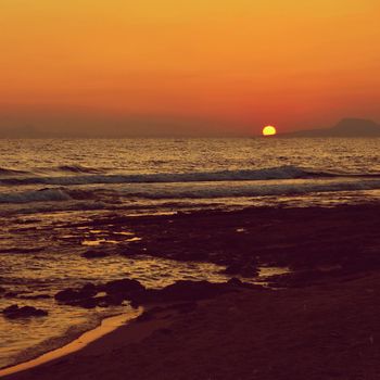 Beautiful summer sunset by the sea. Amazing scenery on the beach with waves and reflection of the sun. Background for holiday and vacation travel. Greece Crete Island.