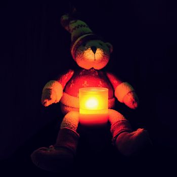 Beautiful Christmas teddy bear sitting with candle. Seasonal winter background for Christmas and holidays. Black clean background with copy space.