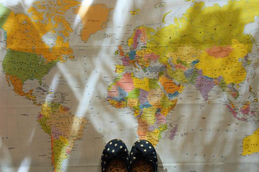 Beautiful concept for summer travel. Small children's shoes on the world map. Planning a summer vacation and holidays.