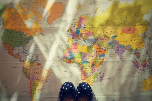 Beautiful concept for summer travel. Small children's shoes on the world map. Planning a summer vacation and holidays.