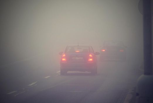 Cars in the fog. Bad winter weather and dangerous automobile traffic on the road. Light vehicles in fog.