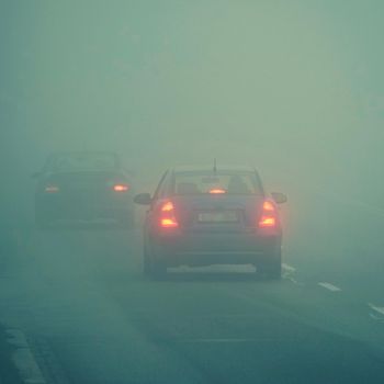 Cars in the fog. Bad winter weather and dangerous automobile traffic on the road. Light vehicles in fog.