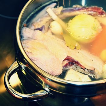 Preparing homemade chicken soup - broth. Pot on the stove in the kitchen with ingredients for cooking.