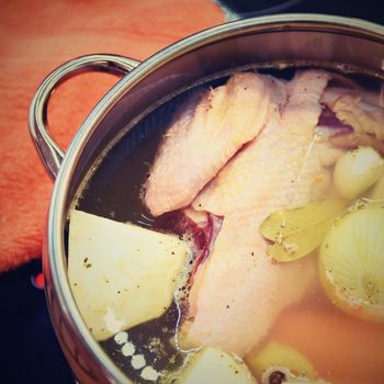 Preparing homemade chicken soup - broth. Pot on the stove in the kitchen with ingredients for cooking.