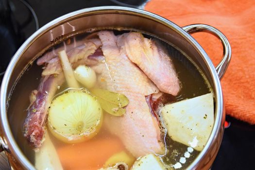 Preparing homemade chicken soup - broth. Pot on the stove in the kitchen with ingredients for cooking.