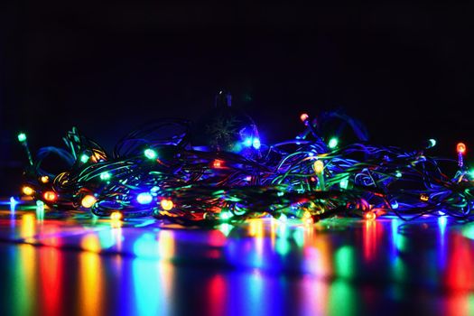 Christmas lights on black background with copy space. Colored reflecting surface.