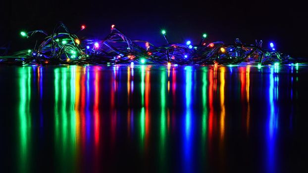 Christmas lights on black background with copy space. Colored reflecting surface.