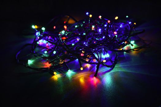 Christmas lights on black background with copy space. Colored reflecting surface.