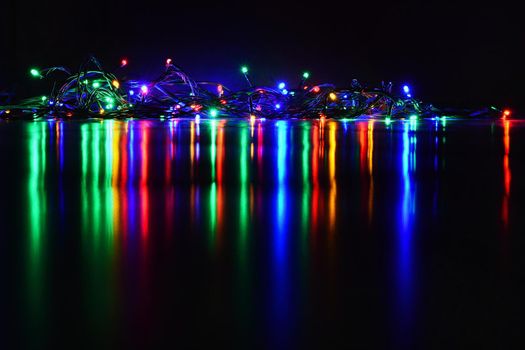 Christmas lights on black background with copy space. Colored reflecting surface.