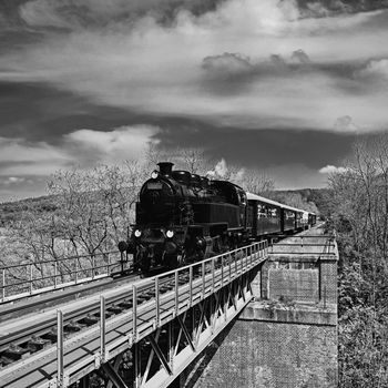 Beautiful old steam train driving along a bridge in the countryside. Concept for travel, transportation and retro old style. Black and white old photo.