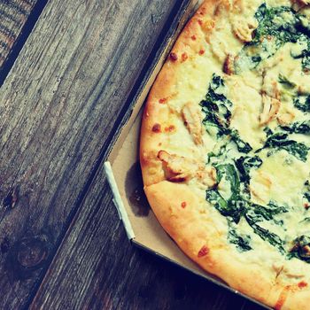 Delicious fresh pizza served on wooden table. Pizza with cream and spinach ready for delivery in a box.