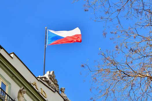 The flag of the Czech Republic on a building with blue sky and the sun in the background.