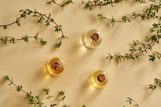 Three bottles of essential oil with fresh thyme on pastel yellow background, top view