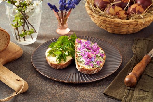 Two slices of bread with butter and wild edible spring plants - goutweed leaves, purple dead-nettle and lungwort flowers