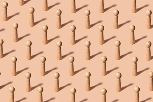 Creative pattern with identical wooden figures representing people on pastel orange background - uniformity concept