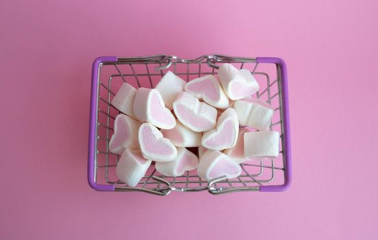 Valentine's Day, top view. Marshmallows pink hearts spilled out of a toy basket on a pink background, copying the space, the concept of love. The concept of buying love