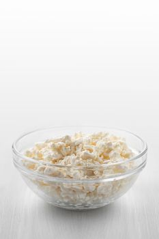 Fresh homemade farm cottage cheese in a glass bowl on a white wooden table. Vertical image.