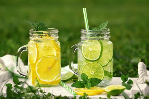 Cold refreshing homemade lemonade with mint, lemon and lime in mason jars on a summer lawn.