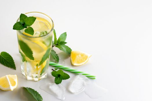 Fresh homemade cocktail with lemon, mint and ice on a white table, copy space.