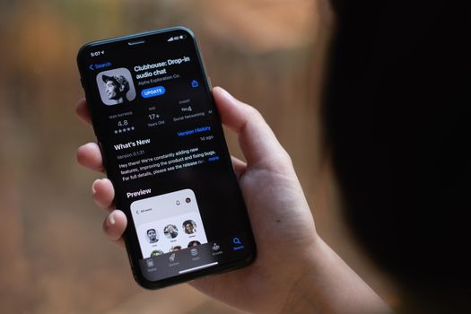 CHIANG MAI, THAILAND, 13 MAR 2021 : Woman in Wired Headphones holding Smartphone with Clubhouse drop in audio chat application on screen. New social network launched in 2020 by Alpha Exploration Co.