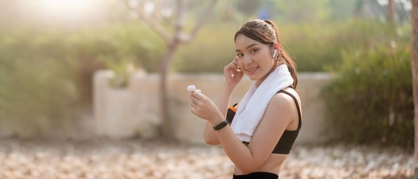 Photo of a beautiful asian young fitness woman running outdoors listening music with earphones.