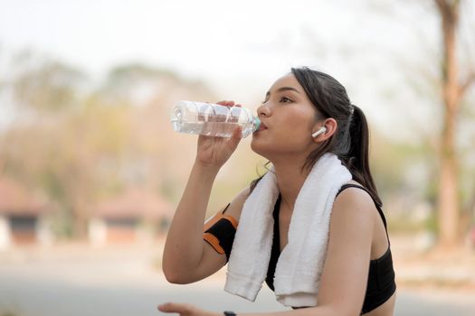 Beautiful fitness athlete woman drinking water after work out exercising on sunrise morning summer in park.