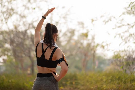 Athletic woman warming up before a workout standing facing the early morning rising sun at park.