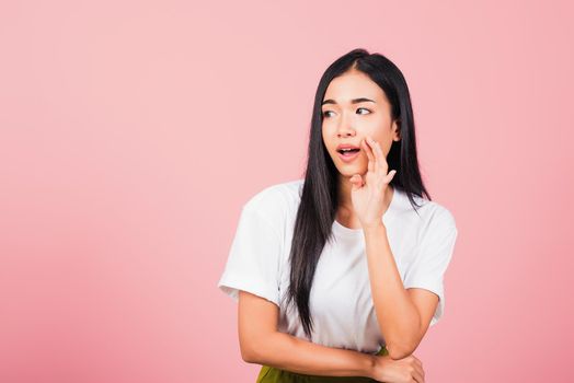 Asian happy portrait beautiful cute young woman teen standing hand on mouth talking whisper secret rumor studio shot isolated on pink background, Thai female looking to side away with copy space