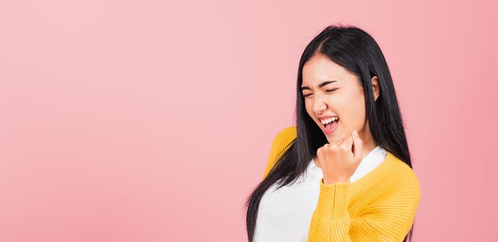 Happy Asian portrait beautiful cute young woman stand makes raised fists up celebrating her winning success gesture, studio shot isolated pink background, Thai female excited say yes! with copy space