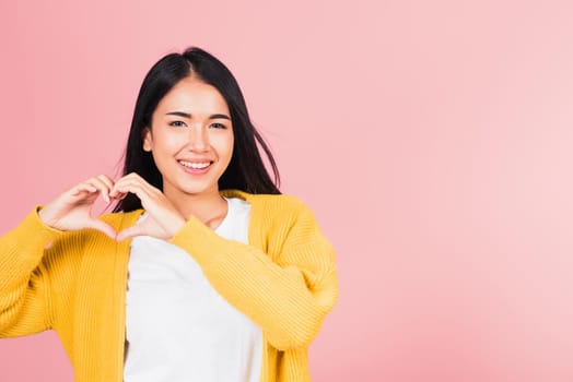 Happy Asian portrait beautiful cute young woman smile make finger heart gesture figure symbol shape sign with two hands sending love to her lover looking camera, studio shot isolated pink background