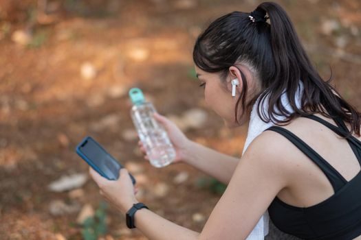 Tired fitness woman sweating taking a break listening to music on phone after difficult training.