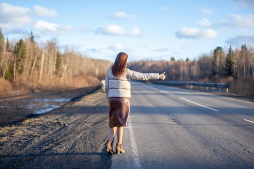 The girl stops the car on the highway with her hand. Stylish woman on the road stops the car go on a journey. A road in the middle of the forest.