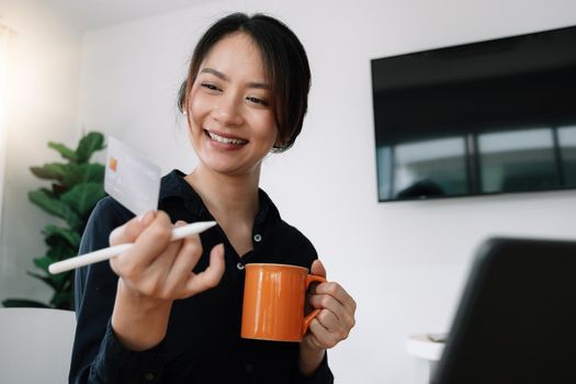 Happy woman holding credit card while using laptop computer for online shopping at home.