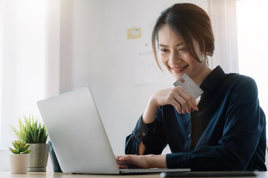 Happy woman holding credit card while using laptop computer for online shopping at home.