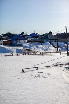 Lots of snow after a snow storm in winter. Houses in the snow captivity. The wooden fence near the houses is covered with snow.