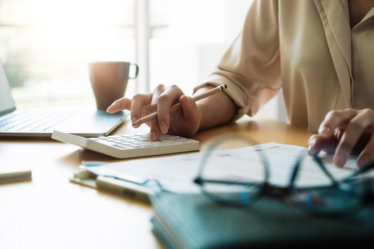 Close up female accountant analyzing financial graph data using calculator to calculate data work from home.