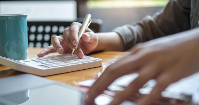 Close up Hands of businesswoman or accountant holding pen and working on calculator to calculate business data, Accountancy document and laptop computer at office, Business concept.