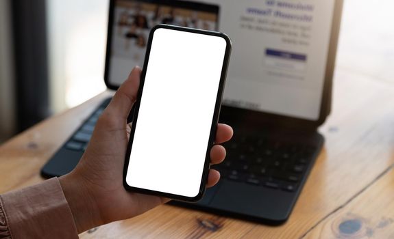 Top view Woman sitting on work desk and holding blank screen mock up mobile phone